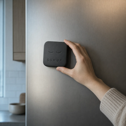 A hand placing the Sunup Block on a fridge door, out of reach of the bedroom